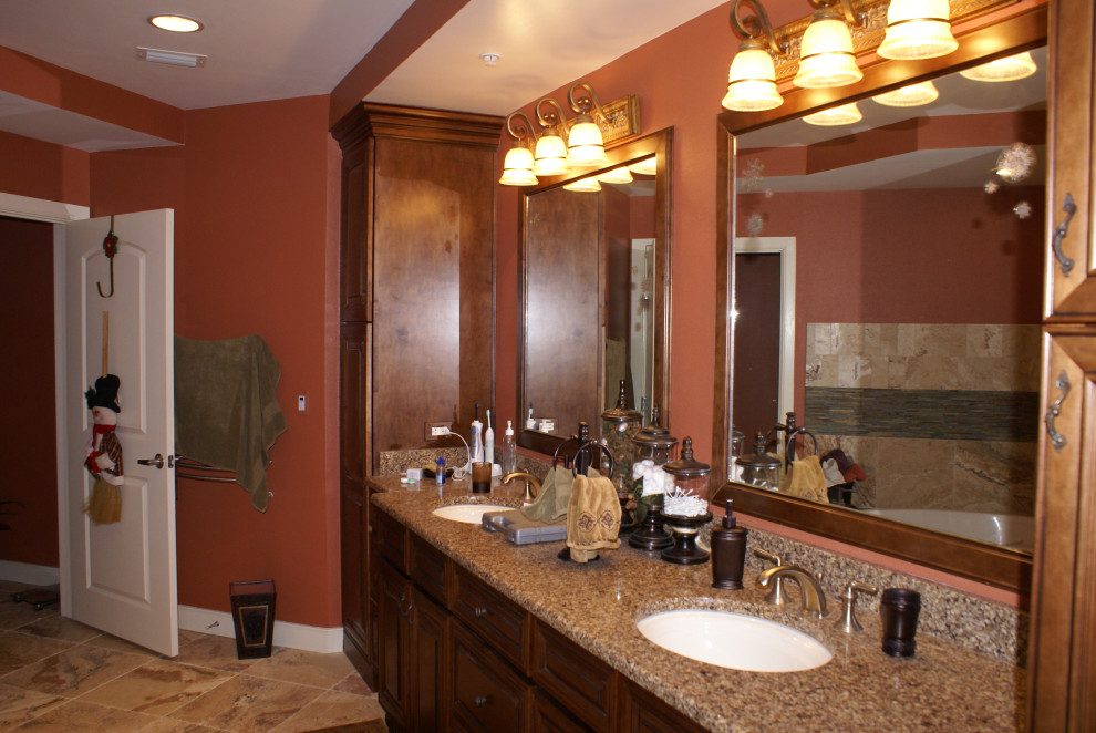 This is an example of a mid-sized mediterranean master bathroom in Other with raised-panel cabinets, medium wood cabinets, a corner shower, beige tile, porcelain tile, orange walls, porcelain floors, an undermount sink, granite benchtops, brown floor, a hinged shower door and brown benchtops.
