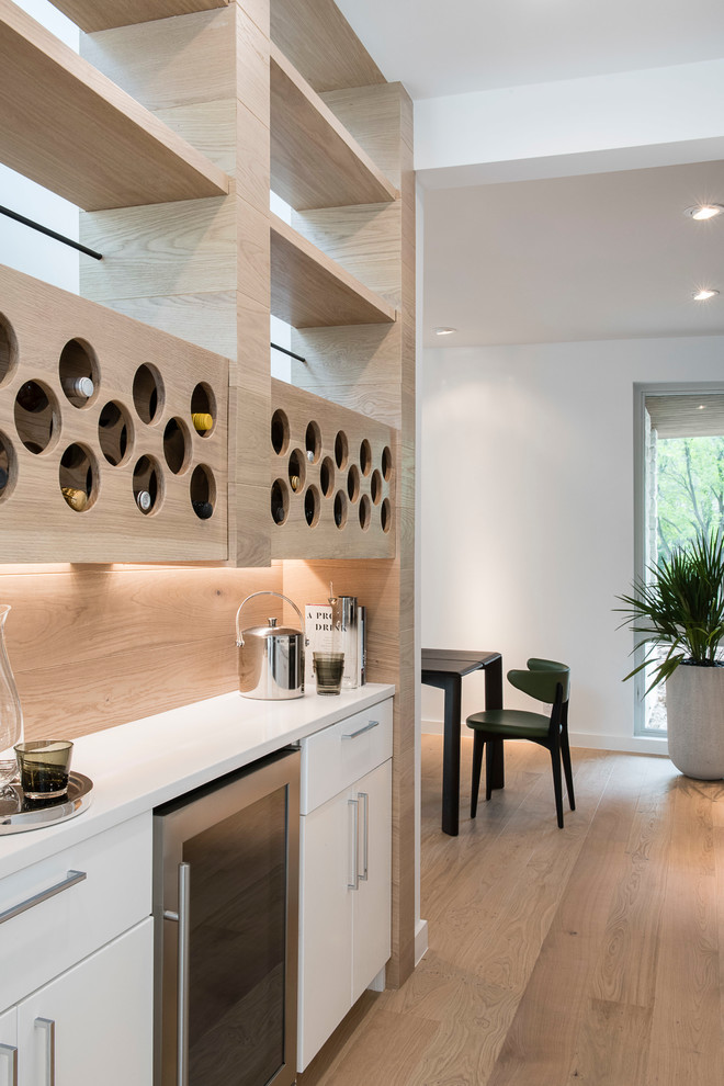 This is an example of a mid-sized contemporary single-wall home bar in Austin with no sink, flat-panel cabinets, white cabinets, solid surface benchtops, timber splashback, white benchtop and light hardwood floors.