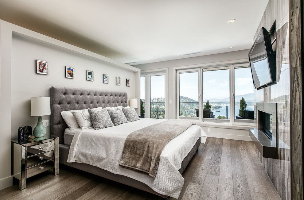 Inspiration for a contemporary master bedroom in Vancouver with grey walls, dark hardwood floors, a two-sided fireplace, a tile fireplace surround and brown floor.