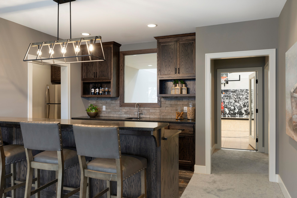 This is an example of a mid-sized transitional u-shaped seated home bar in Minneapolis with an undermount sink, shaker cabinets, dark wood cabinets, granite benchtops, brown splashback, subway tile splashback, ceramic floors, multi-coloured floor and black benchtop.