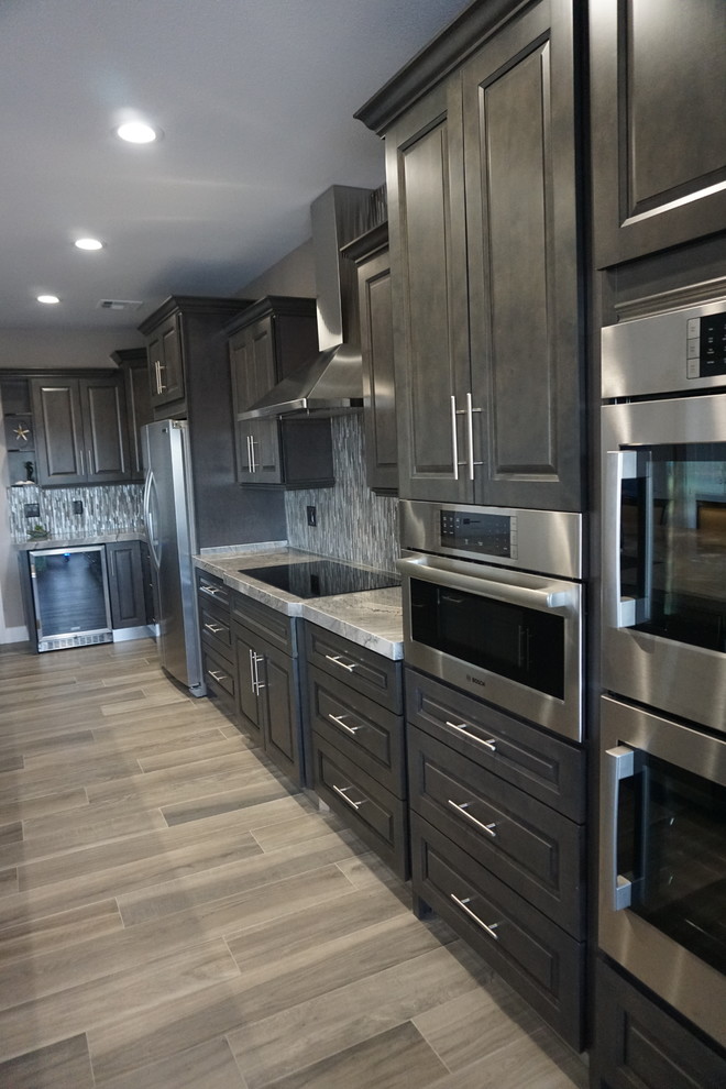Design ideas for a large modern l-shaped eat-in kitchen in Las Vegas with an undermount sink, raised-panel cabinets, grey cabinets, granite benchtops, grey splashback, mosaic tile splashback, stainless steel appliances, ceramic floors, with island, grey floor and grey benchtop.