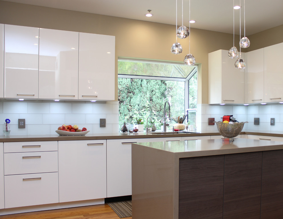 Inspiration for a contemporary u-shaped eat-in kitchen in San Francisco with a single-bowl sink, flat-panel cabinets, white cabinets, quartz benchtops, white splashback, glass tile splashback, stainless steel appliances, medium hardwood floors and with island.