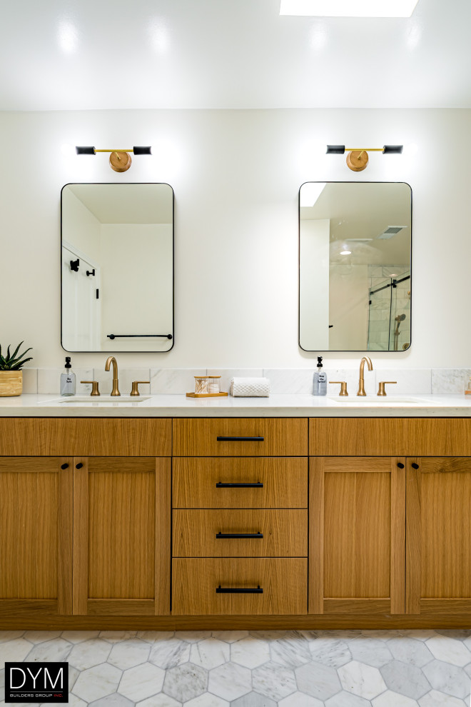 Photo of a large retro ensuite bathroom in Los Angeles with shaker cabinets, medium wood cabinets, a freestanding bath, a corner shower, a one-piece toilet, white tiles, cement tiles, white walls, porcelain flooring, a built-in sink, marble worktops, grey floors, a sliding door, white worktops, a shower bench, double sinks, a built in vanity unit, a wallpapered ceiling and wallpapered walls.