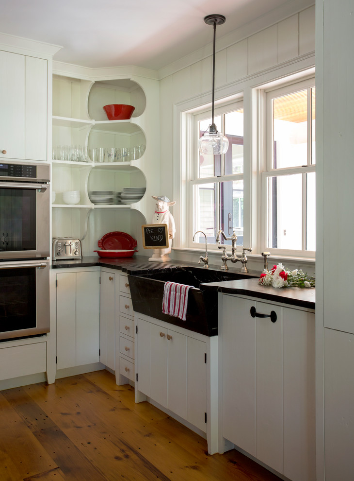 Inspiration for a mid-sized country kitchen in Boston with a farmhouse sink, white cabinets, soapstone benchtops, stainless steel appliances, light hardwood floors, with island and white splashback.