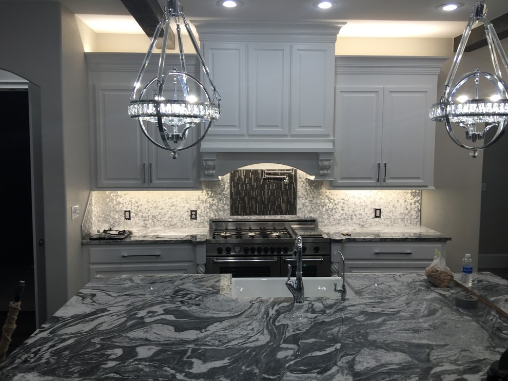 Example of a mid-sized transitional l-shaped dark wood floor and brown floor open concept kitchen design in Orange County with a farmhouse sink, raised-panel cabinets, white cabinets, marble countertops, metallic backsplash, metal backsplash, stainless steel appliances and an island