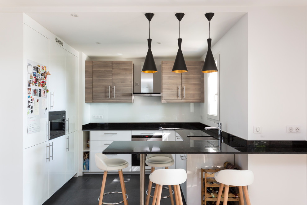 This is an example of a mid-sized modern u-shaped open plan kitchen in Paris with a peninsula, an undermount sink, flat-panel cabinets, white cabinets, granite benchtops, stone slab splashback, stainless steel appliances, ceramic floors, black floor, black benchtop and black splashback.