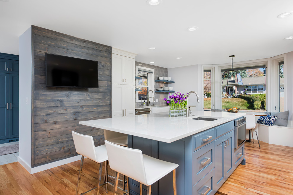 Large transitional u-shaped light wood floor enclosed kitchen photo in Denver with a farmhouse sink, shaker cabinets, white cabinets, quartz countertops, gray backsplash, ceramic backsplash, stainless steel appliances and an island