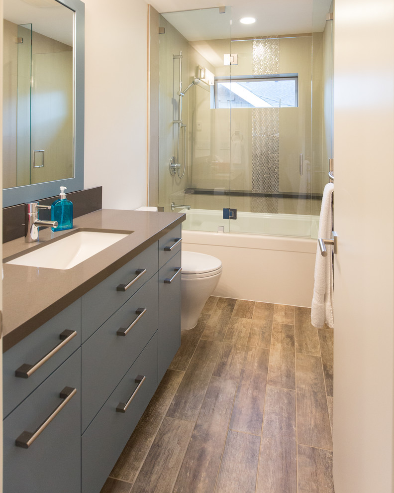 Photo of a large contemporary kids bathroom in Vancouver with an undermount sink, flat-panel cabinets, grey cabinets, engineered quartz benchtops, a freestanding tub, a shower/bathtub combo, a two-piece toilet, white walls and porcelain floors.