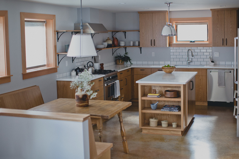 This is an example of a mid-sized transitional l-shaped eat-in kitchen in Portland with an undermount sink, shaker cabinets, light wood cabinets, quartz benchtops, white splashback, porcelain splashback, stainless steel appliances, concrete floors and with island.