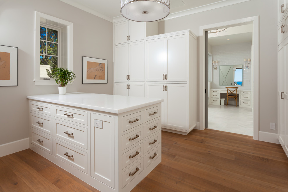 Inspiration for a beach style gender-neutral walk-in wardrobe in Orange County with shaker cabinets, white cabinets and light hardwood floors.
