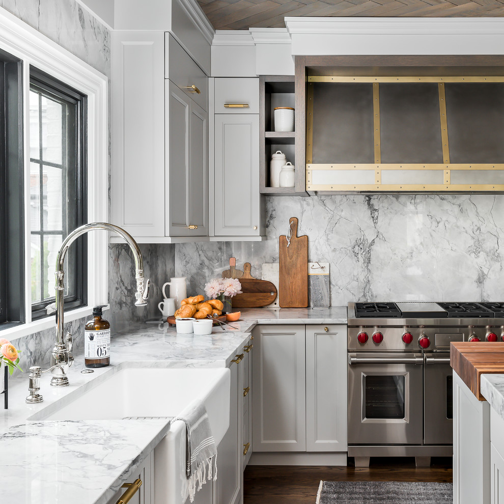 Example of a mid-sized transitional medium tone wood floor and brown floor enclosed kitchen design in Chicago with a farmhouse sink, recessed-panel cabinets, gray cabinets, quartzite countertops, gray backsplash, stone slab backsplash, paneled appliances, an island and gray countertops