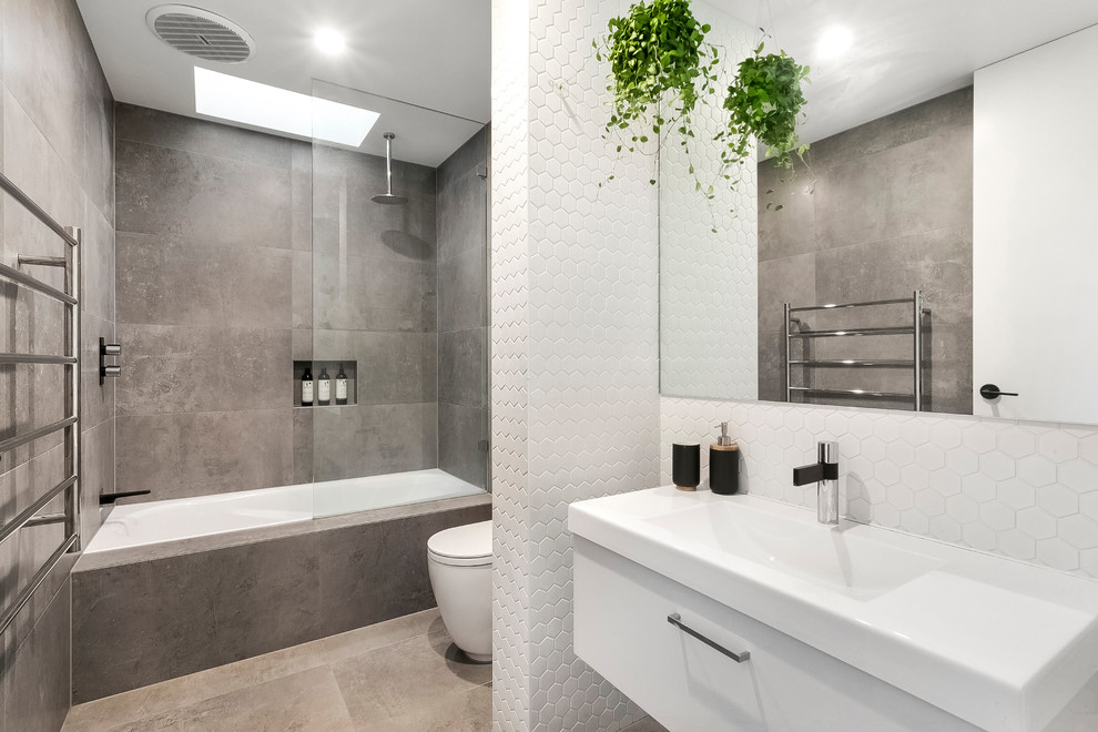 This is an example of a contemporary master bathroom with an undermount tub, a shower/bathtub combo, gray tile, an integrated sink, flat-panel cabinets, white cabinets, a one-piece toilet, grey walls, an open shower, ceramic tile, ceramic floors and grey floor.
