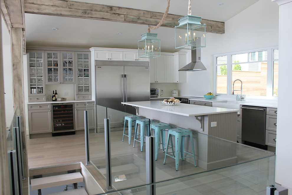 Design ideas for a mid-sized beach style u-shaped eat-in kitchen in Vancouver with a farmhouse sink, shaker cabinets, grey cabinets, solid surface benchtops, stainless steel appliances, light hardwood floors, with island and grey floor.