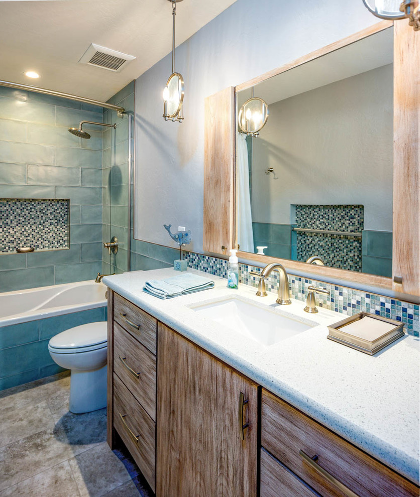 This is an example of a beach style 3/4 bathroom in Phoenix with flat-panel cabinets, distressed cabinets, an alcove tub, a shower/bathtub combo, a two-piece toilet, blue tile, glass tile, blue walls, an undermount sink, brown floor, a shower curtain and grey benchtops.