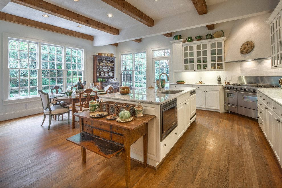 This is an example of a large traditional l-shaped eat-in kitchen in Atlanta with white cabinets, with island, an undermount sink, glass-front cabinets, granite benchtops, white splashback, stainless steel appliances and medium hardwood floors.