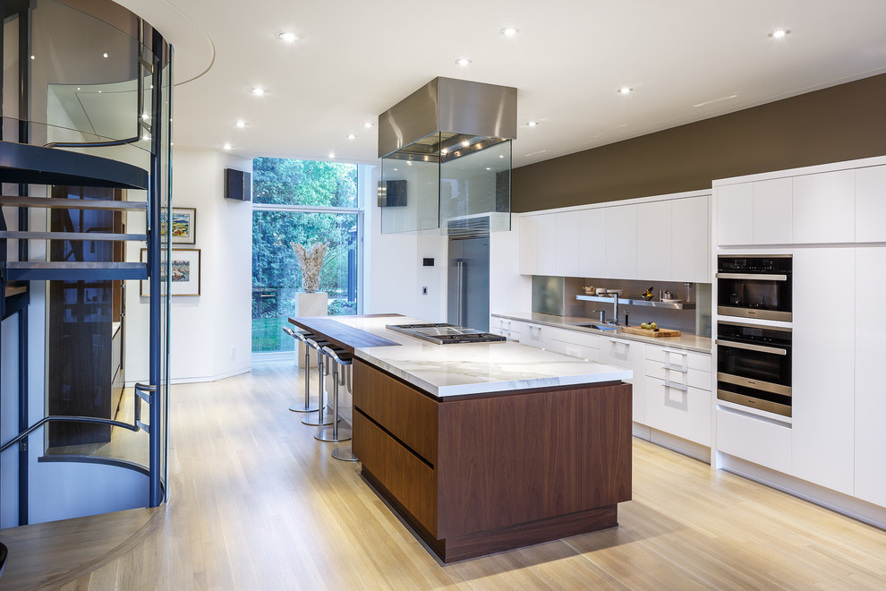 This is an example of a large contemporary galley eat-in kitchen in Ottawa with an undermount sink, flat-panel cabinets, white cabinets, wood benchtops, grey splashback, stone slab splashback, stainless steel appliances, light hardwood floors and with island.