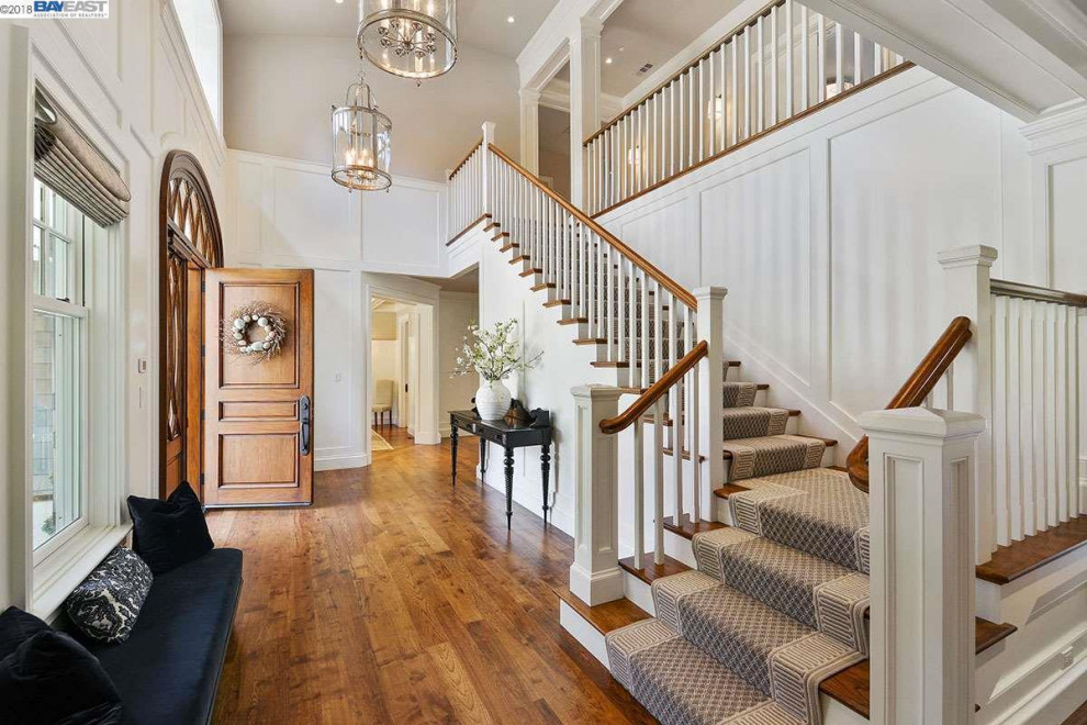 Design ideas for a large traditional foyer in San Francisco with white walls, medium hardwood floors, a single front door, brown floor, vaulted, decorative wall panelling and a medium wood front door.