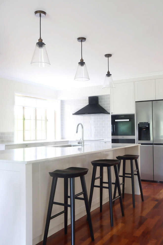 Inspiration for a mid-sized traditional l-shaped open plan kitchen in Other with a double-bowl sink, shaker cabinets, white cabinets, grey splashback, subway tile splashback, black appliances, dark hardwood floors and with island.