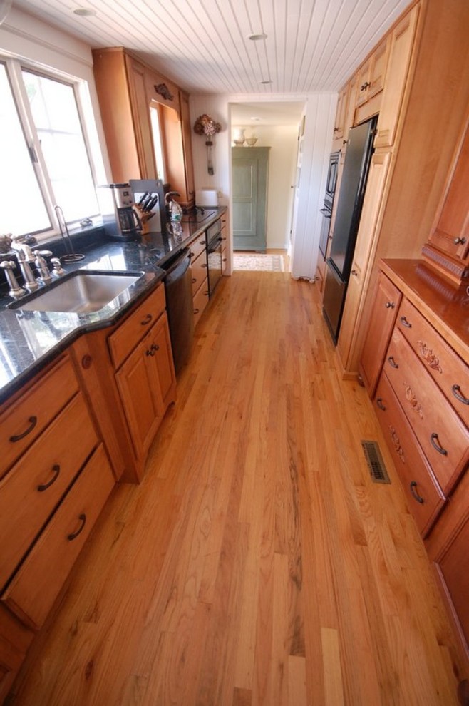 This is an example of a mid-sized traditional galley separate kitchen in New York with an undermount sink, raised-panel cabinets, medium wood cabinets, granite benchtops, medium hardwood floors, no island and black appliances.