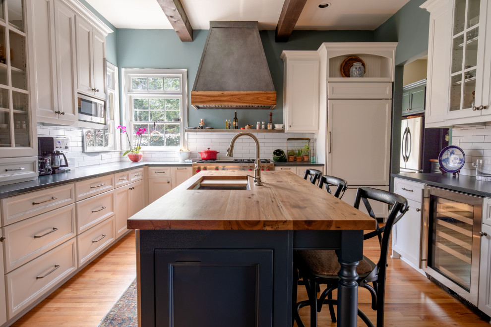 Inspiration for a mid-sized traditional u-shaped kitchen in Atlanta with an undermount sink, white cabinets, white splashback, subway tile splashback, stainless steel appliances, with island, brown floor, recessed-panel cabinets, wood benchtops, medium hardwood floors and brown benchtop.