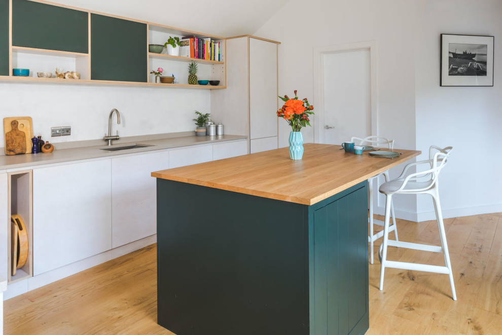 This is an example of a mid-sized contemporary l-shaped open plan kitchen in Oxfordshire with a drop-in sink, flat-panel cabinets, stainless steel appliances, with island, beige benchtop, orange cabinets, wood benchtops, light hardwood floors and beige floor.