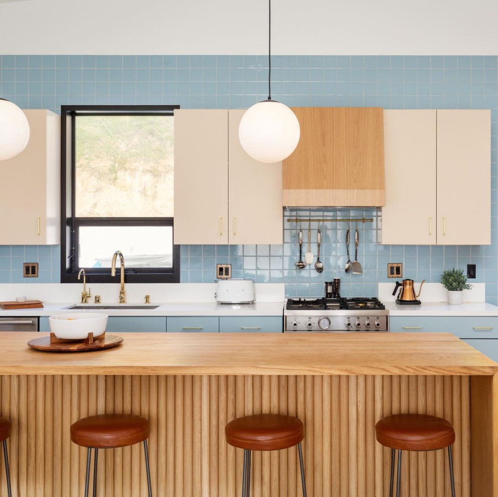 Foto de cocina comedor costera con puertas de armario azules, encimera de madera, salpicadero azul, electrodomésticos de acero inoxidable, suelo de madera en tonos medios, una isla, suelo marrón y encimeras blancas
