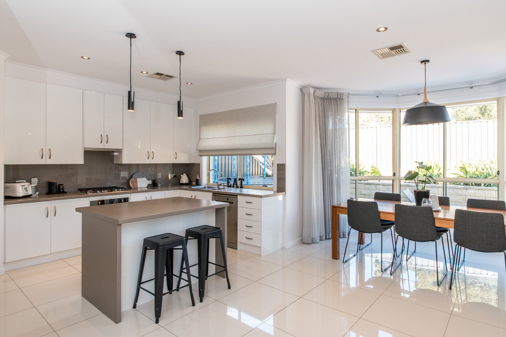 Scandinavian l-shaped eat-in kitchen in Adelaide with a drop-in sink, flat-panel cabinets, white cabinets, beige splashback, glass sheet splashback, stainless steel appliances, with island, white floor and beige benchtop.