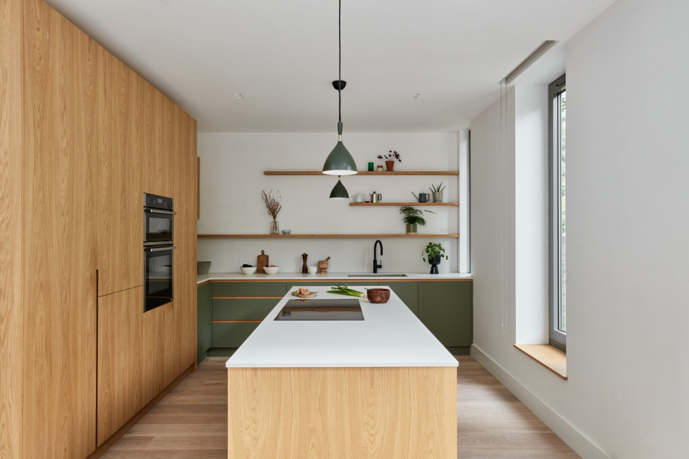 This is an example of a medium sized contemporary l-shaped kitchen/diner in London with a built-in sink, flat-panel cabinets, light wood cabinets, composite countertops, white splashback, engineered quartz splashback, integrated appliances, light hardwood flooring, an island, beige floors and white worktops.