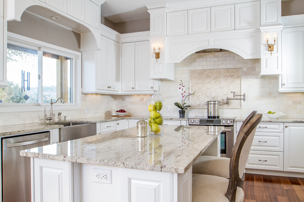 Eat-in kitchen - large transitional l-shaped medium tone wood floor eat-in kitchen idea in Austin with a farmhouse sink, raised-panel cabinets, white cabinets, granite countertops, beige backsplash, ceramic backsplash, stainless steel appliances and an island
