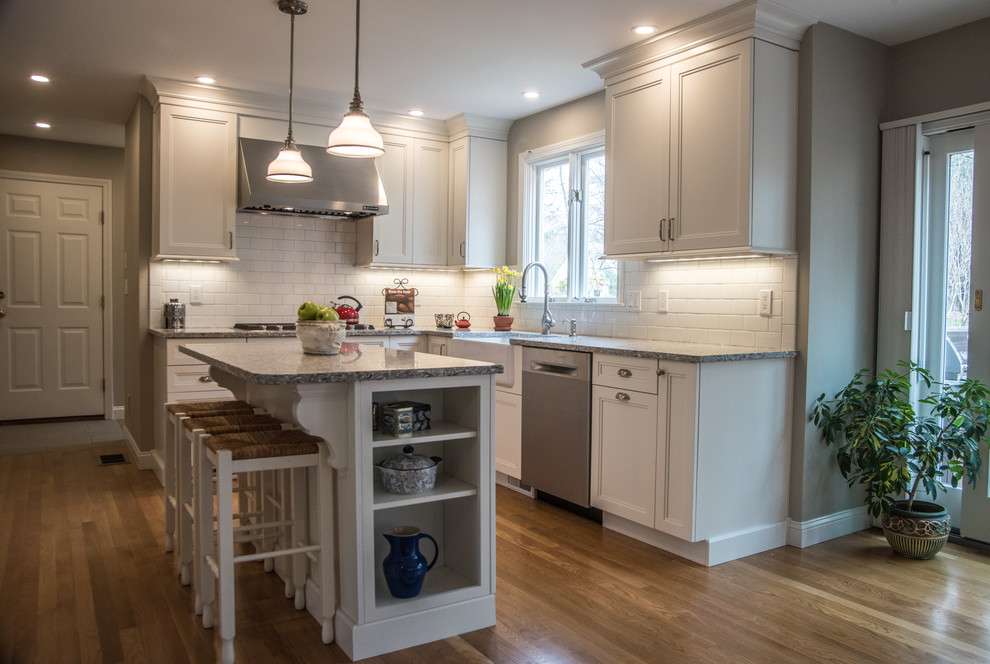 Example of a mid-sized transitional l-shaped medium tone wood floor eat-in kitchen design in Boston with a farmhouse sink, shaker cabinets, white cabinets, quartz countertops, white backsplash, subway tile backsplash, stainless steel appliances and an island