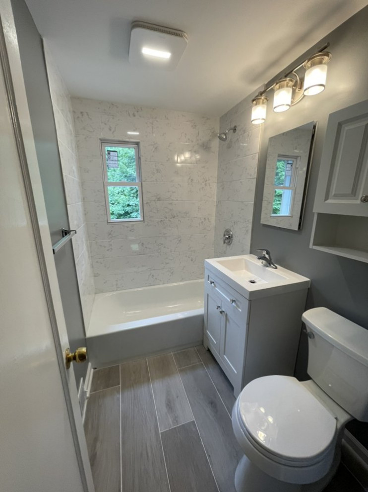 Idées déco pour une petite salle d'eau classique avec un placard à porte shaker, des portes de placard grises, une baignoire posée, un combiné douche/baignoire, un mur gris, un sol en carrelage de porcelaine, une cabine de douche avec un rideau, un plan de toilette blanc, meuble simple vasque et meuble-lavabo sur pied.