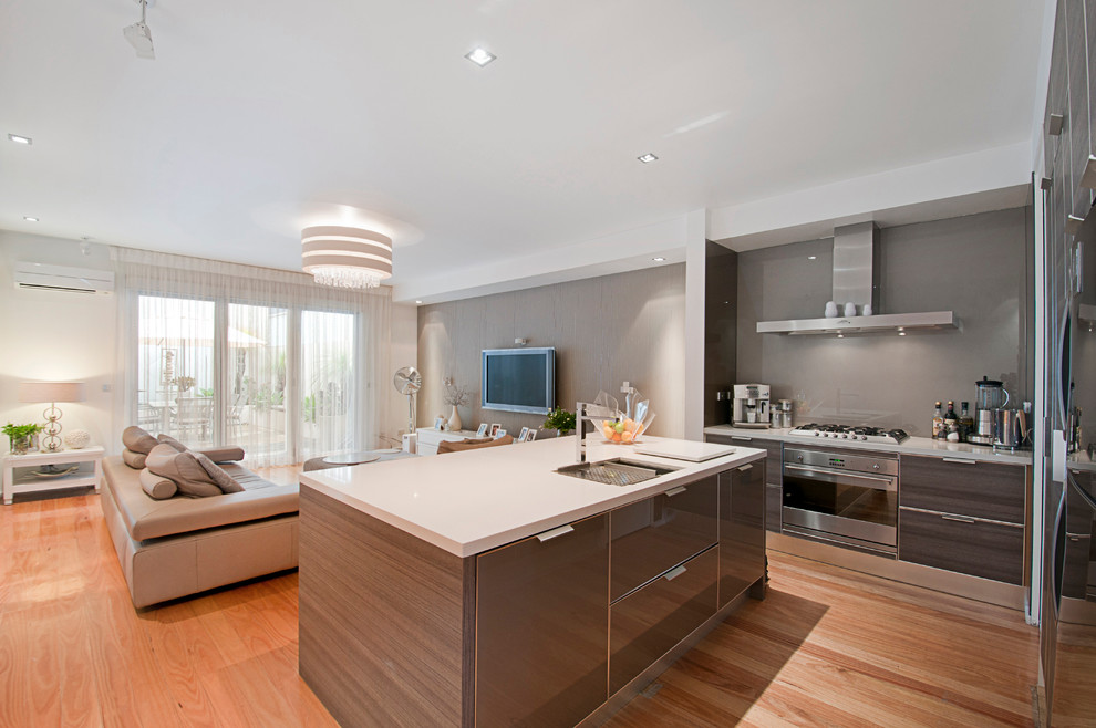 Design ideas for a mid-sized contemporary l-shaped open plan kitchen in Melbourne with an undermount sink, flat-panel cabinets, medium wood cabinets, quartz benchtops, beige splashback, glass tile splashback, stainless steel appliances, light hardwood floors and with island.