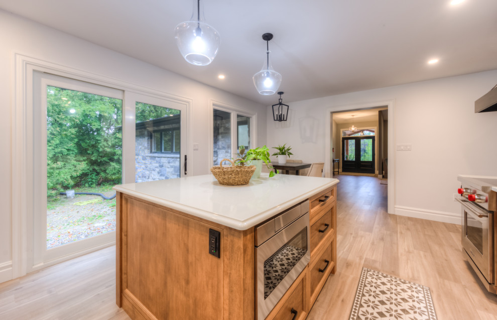 Inspiration for a transitional l-shaped kitchen remodel in Toronto with an undermount sink, shaker cabinets, light wood cabinets, white backsplash, stainless steel appliances, an island and white countertops