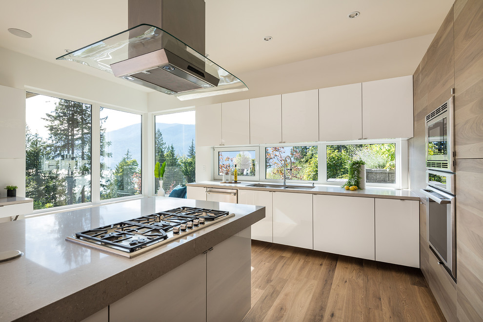 Photo of an expansive contemporary l-shaped eat-in kitchen in Vancouver with an undermount sink, flat-panel cabinets, grey cabinets, quartzite benchtops, window splashback, stainless steel appliances, medium hardwood floors, multiple islands and brown floor.