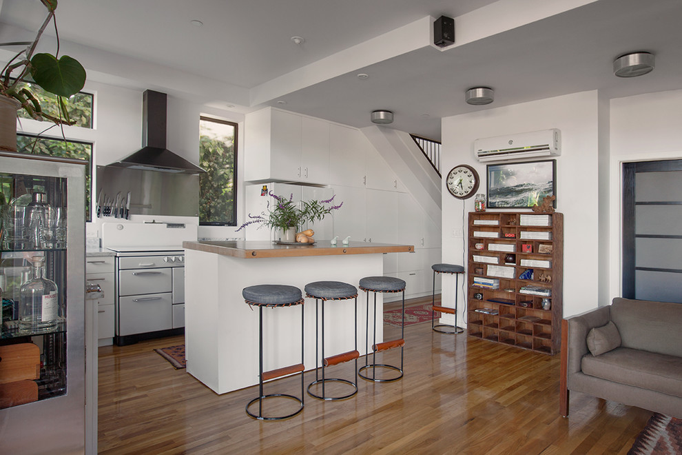 Photo of a modern l-shaped eat-in kitchen in Los Angeles with an undermount sink, flat-panel cabinets, white cabinets, marble benchtops, white splashback, stone slab splashback, white appliances and medium hardwood floors.