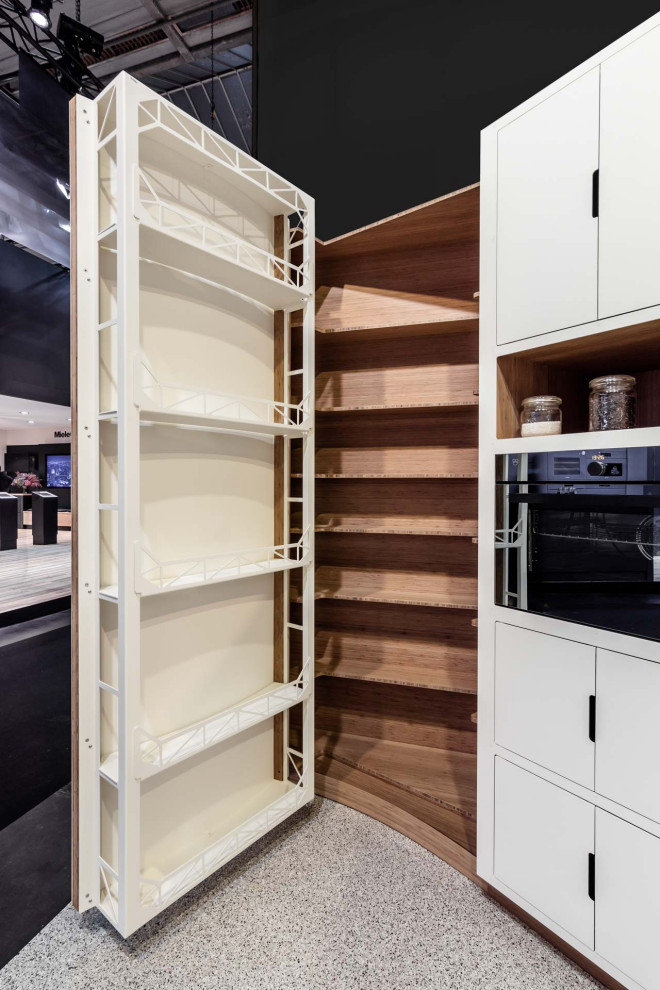 This is an example of a large contemporary l-shaped kitchen pantry in Paris with an undermount sink, beaded inset cabinets, white cabinets, stainless steel benchtops, beige splashback, timber splashback, black appliances, terrazzo floors, a peninsula, grey floor and grey benchtop.