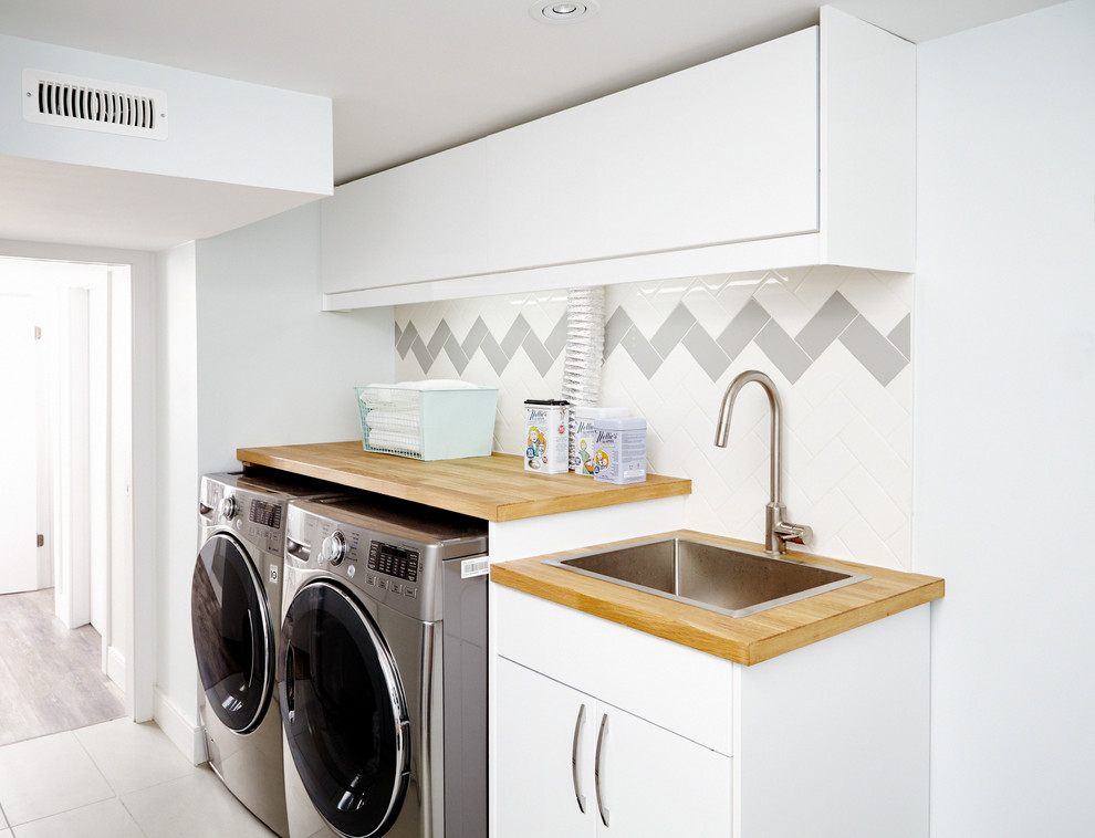 Photo of a scandinavian single-wall dedicated laundry room in Toronto with a drop-in sink, flat-panel cabinets, white cabinets, wood benchtops, white walls, a side-by-side washer and dryer and beige benchtop.