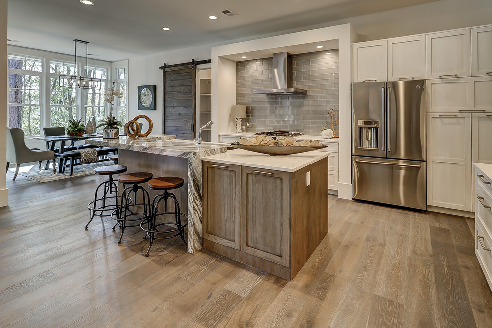 Photo of a large transitional l-shaped eat-in kitchen in Charleston with shaker cabinets, white cabinets, grey splashback, subway tile splashback, stainless steel appliances, medium hardwood floors, with island, brown floor, white benchtop and quartz benchtops.