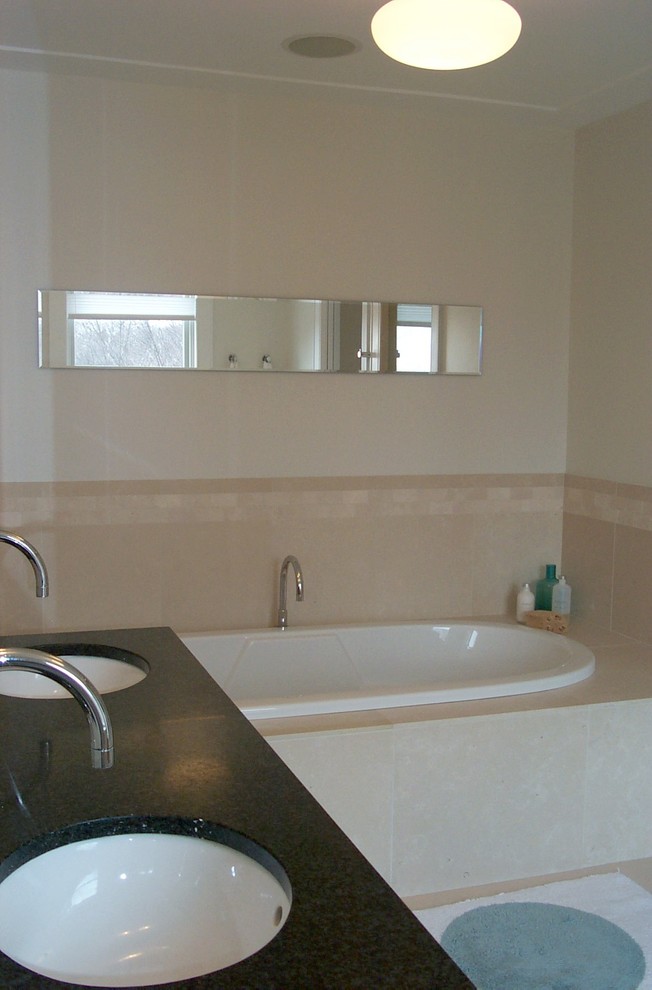Mid-sized modern master bathroom in New York with a drop-in tub, beige tile, stone tile, beige walls, limestone floors, granite benchtops, flat-panel cabinets, medium wood cabinets, an undermount sink, beige floor, black benchtops, a double vanity, a freestanding vanity and recessed.