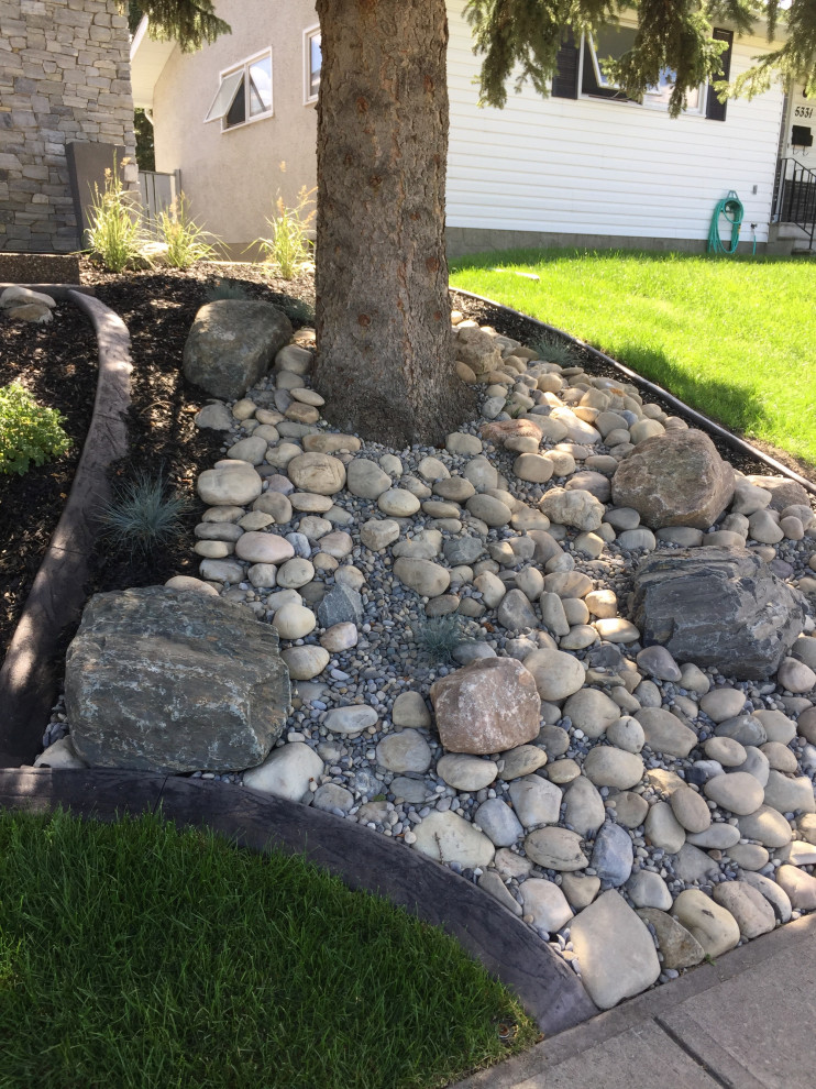 This is an example of a mid-sized front yard formal garden in Calgary with with rock feature and river rock.