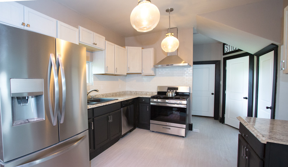 Example of a mid-sized transitional l-shaped vinyl floor and white floor enclosed kitchen design with a double-bowl sink, recessed-panel cabinets, black cabinets, laminate countertops, white backsplash, subway tile backsplash, stainless steel appliances and gray countertops