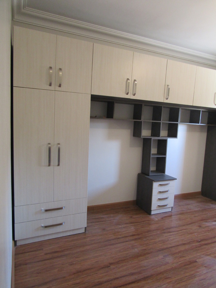 Inspiration for a large modern gender-neutral built-in wardrobe in Other with flat-panel cabinets, beige cabinets, laminate floors and brown floor.