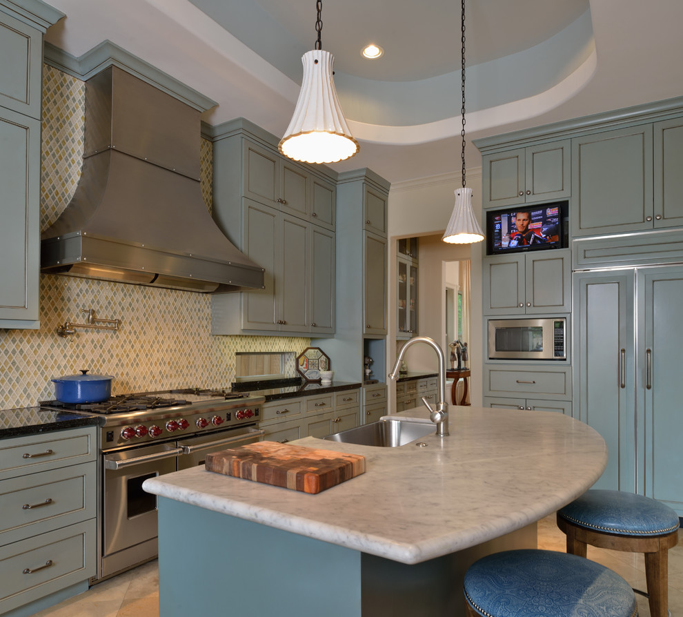 Design ideas for a large traditional l-shaped kitchen in Houston with a farmhouse sink, raised-panel cabinets, blue cabinets, granite benchtops, multi-coloured splashback, porcelain splashback, panelled appliances, travertine floors and with island.