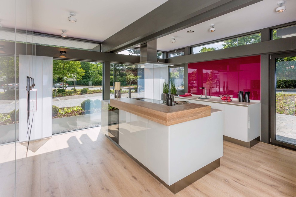 Küche mit Glasfronten, weißen Schränken, hellem Holzboden, Kücheninsel, braunem Boden, Einbauwaschbecken, Mineralwerkstoff-Arbeitsplatte, Küchenrückwand in Weiß, Rückwand aus Holz, schwarzen Elektrogeräten und weißer Arbeitsplatte in Stuttgart