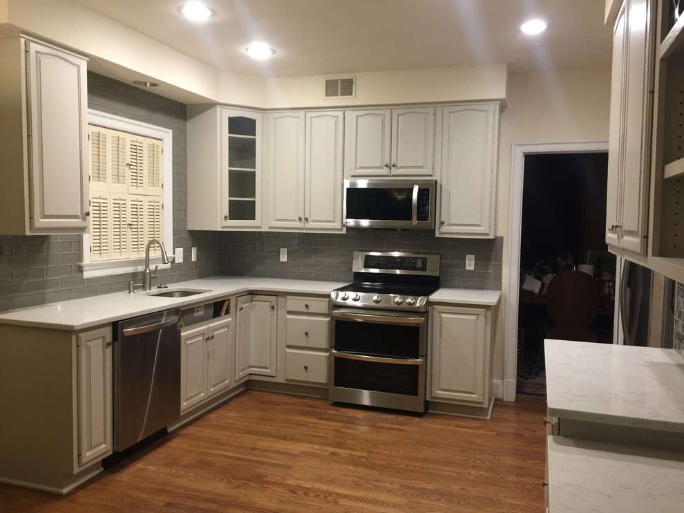 Photo of a mid-sized transitional u-shaped eat-in kitchen in DC Metro with an undermount sink, raised-panel cabinets, grey cabinets, quartz benchtops, grey splashback, glass tile splashback, stainless steel appliances and medium hardwood floors.