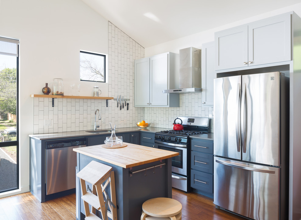 Photo of a small transitional l-shaped kitchen in Austin with an undermount sink, soapstone benchtops, white splashback, subway tile splashback, stainless steel appliances, medium hardwood floors, with island, shaker cabinets, blue cabinets and orange floor.