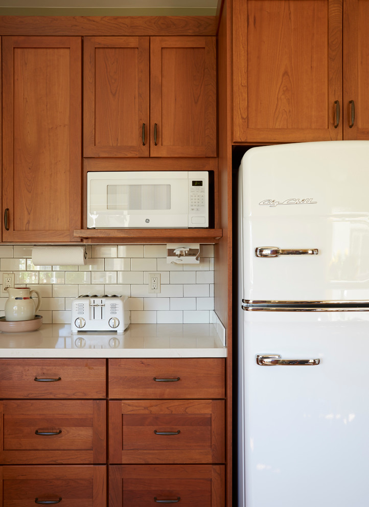 This is an example of a mid-sized arts and crafts separate kitchen in San Francisco with an undermount sink, shaker cabinets, medium wood cabinets, quartz benchtops, white splashback, ceramic splashback, white appliances and medium hardwood floors.