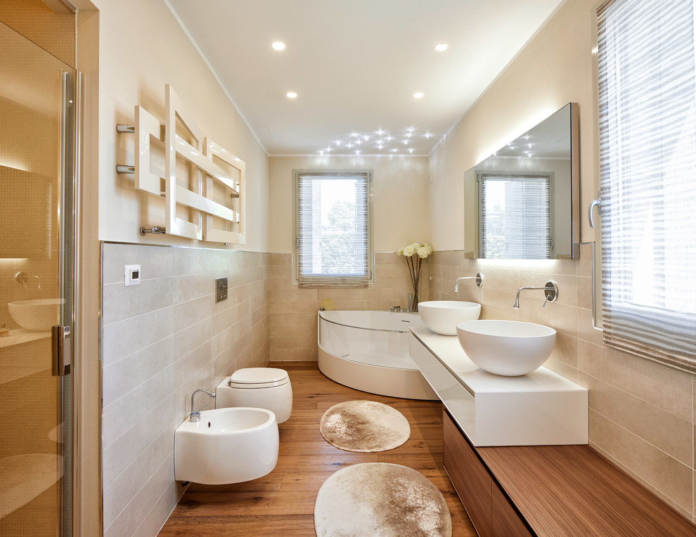 Photo of a contemporary master bathroom in Other with flat-panel cabinets, white cabinets, a corner tub, a vessel sink, a bidet, beige tile, beige walls, medium hardwood floors, brown floor and white benchtops.