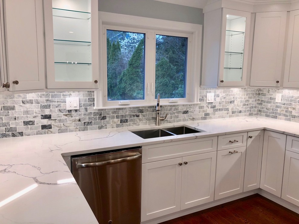 Example of a mid-sized transitional u-shaped dark wood floor and brown floor enclosed kitchen design with an undermount sink, shaker cabinets, white cabinets, marble countertops, gray backsplash, stone tile backsplash, stainless steel appliances, no island and white countertops