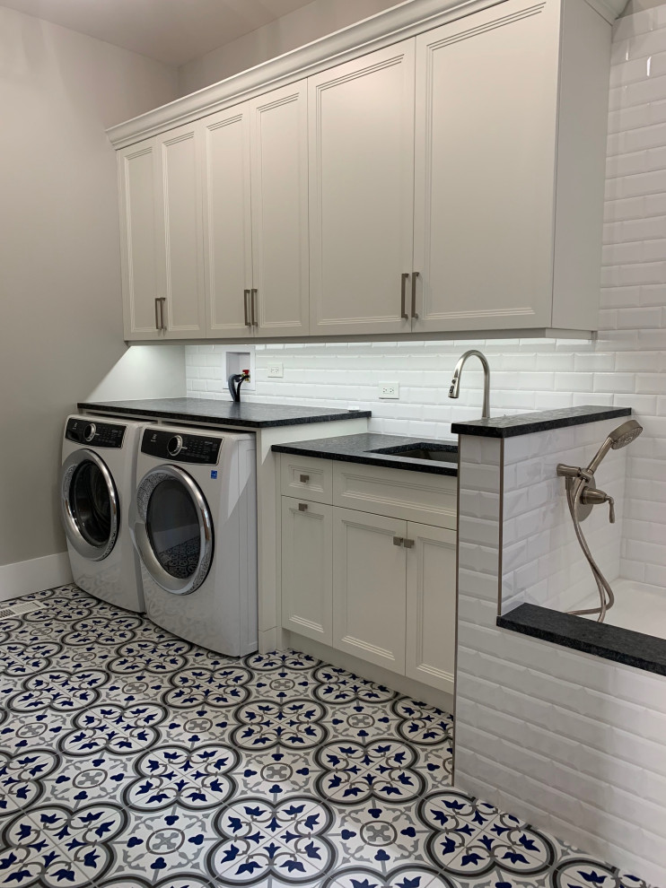 Photo of a mid-sized traditional laundry room in Chicago with an undermount sink, flat-panel cabinets, white cabinets, granite benchtops, white splashback, subway tile splashback, grey walls, ceramic floors, a side-by-side washer and dryer, multi-coloured floor and black benchtop.